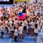 <p><span style="color: #000000;"> Dziecięce drużyny sportowe na hali sportowej. Na pierwszym planie postać dużego, pluszowego Chrumasa otoczonego dziećmi </span></p>