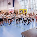 <p><span style="color: #000000;"> Dzieci gimnastykujące się na hali sportowej pod okiem trenerki. Na pierwszym planie Monika Pyrek – mistrzyni i rekordzistka Polski i Europy w skoku o tyczce, medalistka mistrzostw świata, olimpijka, </span></p>
